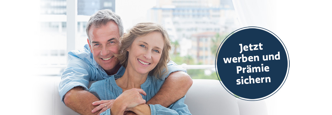 Content man hugging his wife on the couch smiling at camera at home in the living room